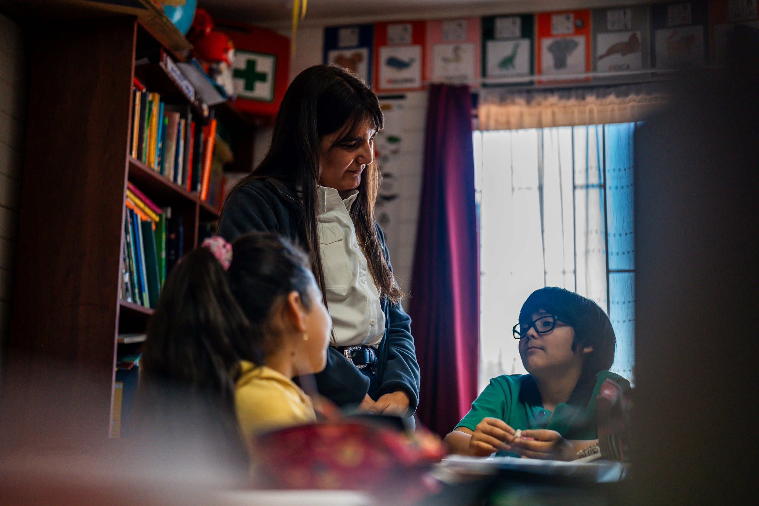 Educadora conversa con una niña y un niño en una sala con libros